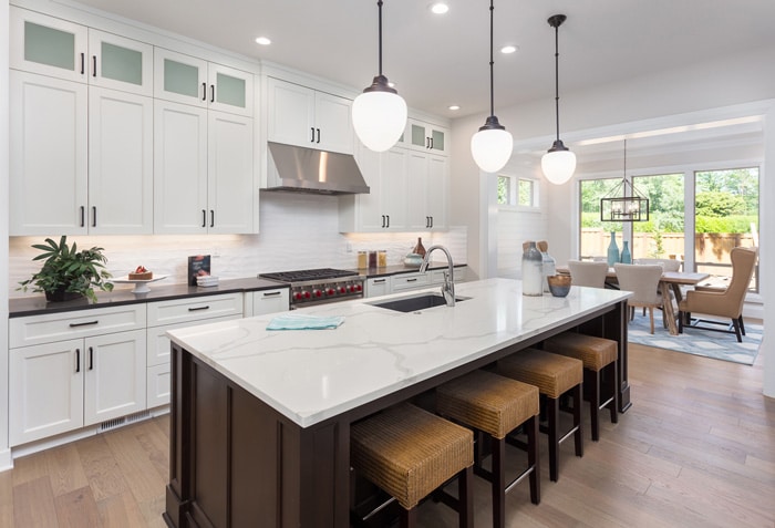 A modern kitchen featuring white cabinetry, a large island with seating, and stylish pendant lights, creating an inviting and functional space.
