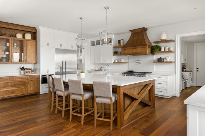 Modern kitchen featuring white cabinetry, wooden accents, a large island with seating, and high-end appliances, complemented by warm wooden flooring.